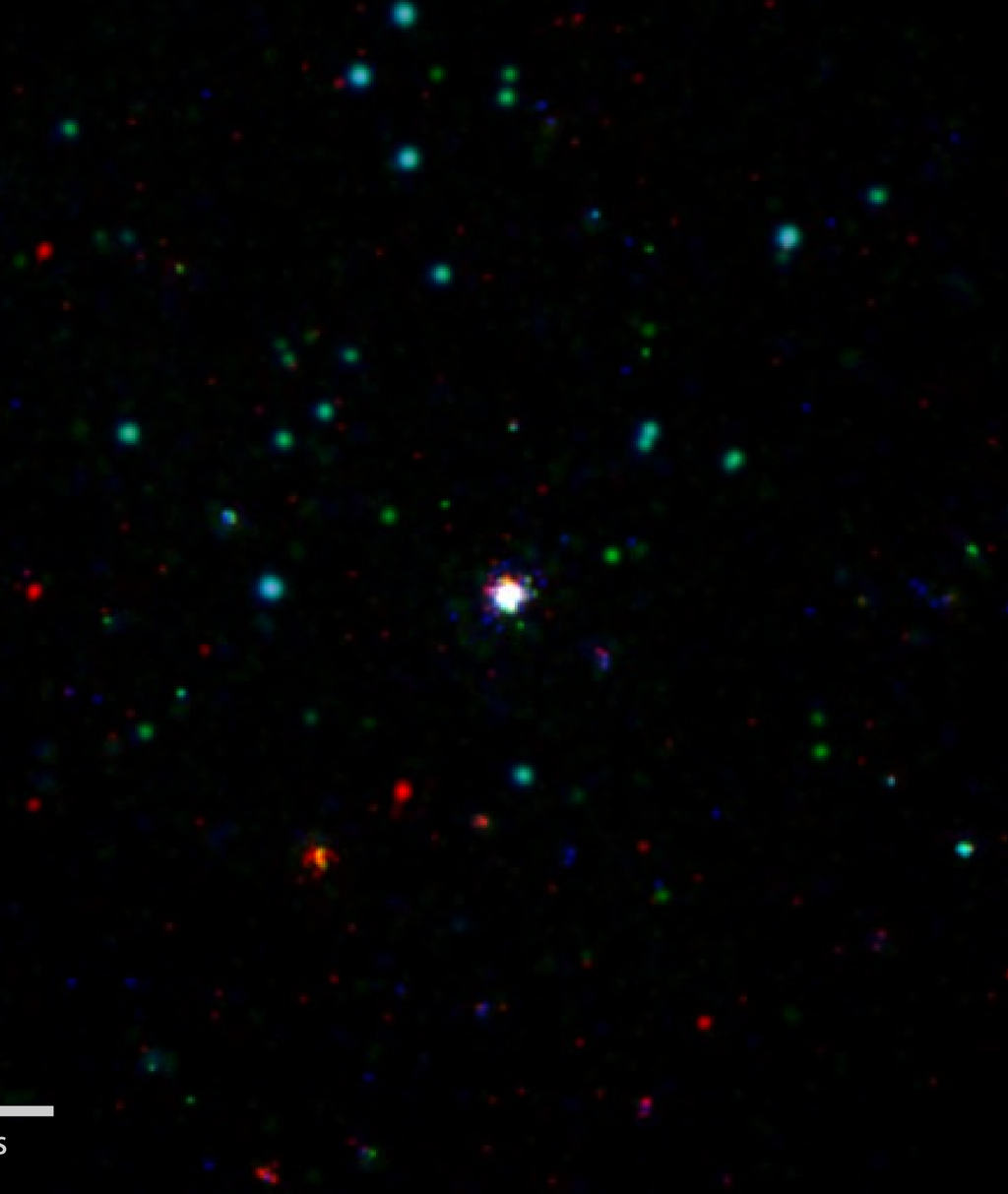 Labeled image. GRB 151027B, Swift's 1,000th burst (center), is shown in this composite X-ray, ultraviolet and optical image. X-rays were captured by Swift's X-Ray Telescope, which began observing the field 3.4 minutes after the Burst Alert Telescope detected the blast. Swift's Ultraviolet/Optical Telescope (UVOT) began observations seven seconds later and faintly detected the burst in visible light. The image includes X-rays with energies from 300 to 6,000 electron volts, primarily from the burst, and lower-energy light seen through the UVOT's visible, blue and ultraviolet filters (shown, respectively, in red, green and blue). The image has a cumulative exposure of 10.4 hours.  Credit: NASA/Swift/Phil Evans, Univ. of Leicester
