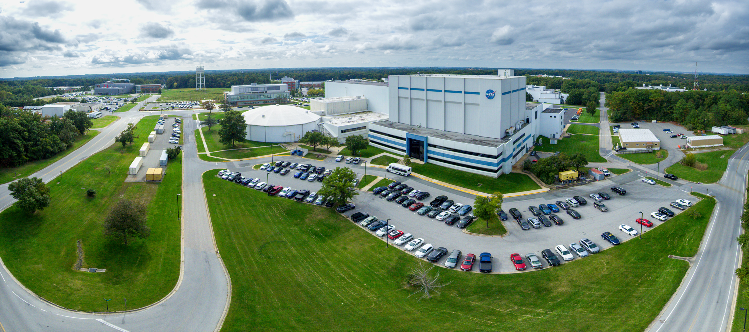 Building 29, home of the largest high-bay clean room in the world, stands prominently in this panoramic aerial view of NASA's Goddard Space Flight Center in Greenbelt, Maryland. The clean room is as tall as an eight-story building and as wide as two basketball courts. The circular structure left of center houses the High Capacity Centrifuge, which is used to simulate launch and landing loads on spacecraft hardware. Imaged Oct. 5, 2023, looking south-southwest.Credit: NASA/Francis Reddy